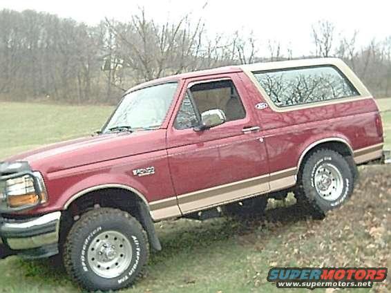 1994 Ford Bronco, red with tan trim, parked on a grassy incline