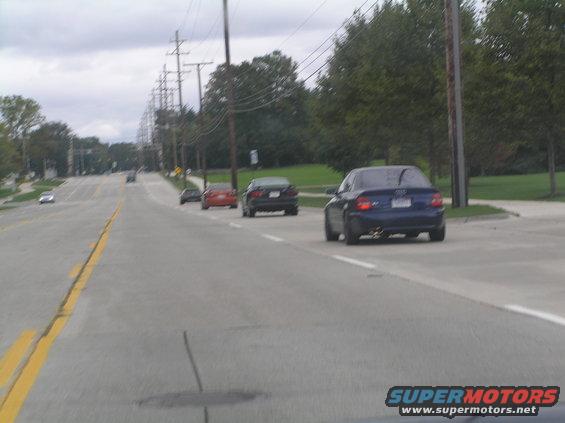 Several cars driving on a road, one blue sedan in the foreground