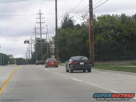 Black coupe, rear view, driving on a road with railroad crossing
