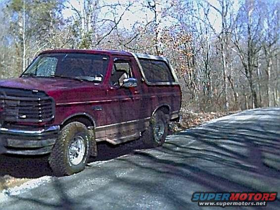 Red Ford Bronco parked on a dirt road with trees in the background