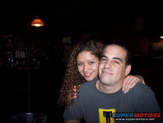 Couple posing for a photo in a bar or restaurant, with a "SUPERMOTORS.NET" watermark visible