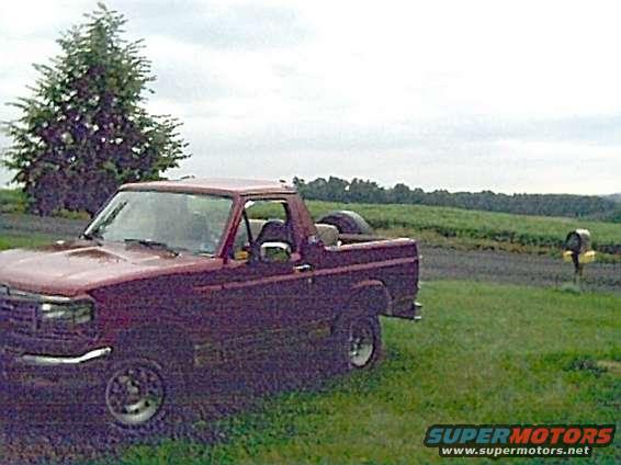Maroon pickup truck parked in a grassy field with a tree and mailbox nearby
