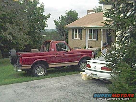 Red Ford Bronco with spare tire on rear, parked on grass next to a house