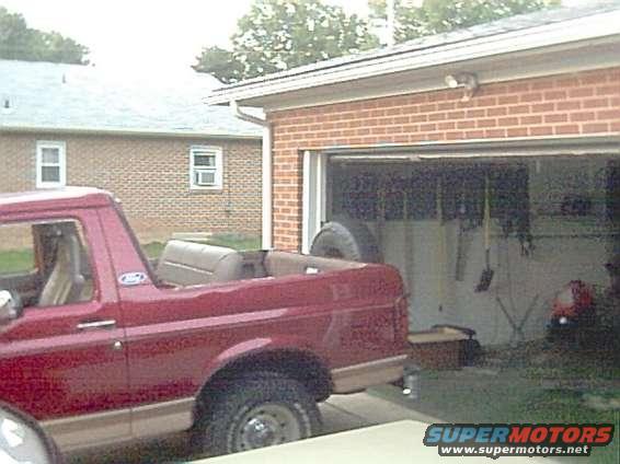 Red 1994 Ford Bronco with top removed, parked next to a garage