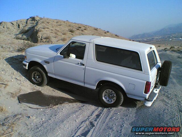 White 1996 Ford Bronco parked on a sandy, hilly terrain with mountains in the background