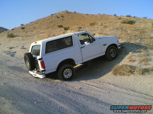 White Ford Bronco driving up a dirt hill, spare tire mounted on the back