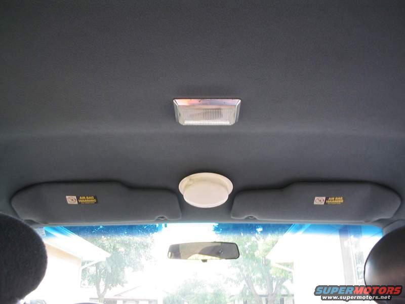 Car interior ceiling with two sun visors, a dome light, and a rectangular interior light. Air bag warning labels are visible on the visors