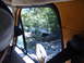 1988 Ford Bronco - A blue SUV is seen tilted off-road in a wooded area, with a spare tire mounted on the back.