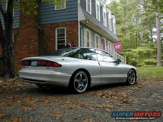 Silver 1993 Ford Probe coupe parked in front of a brick and blue house, rear-left view