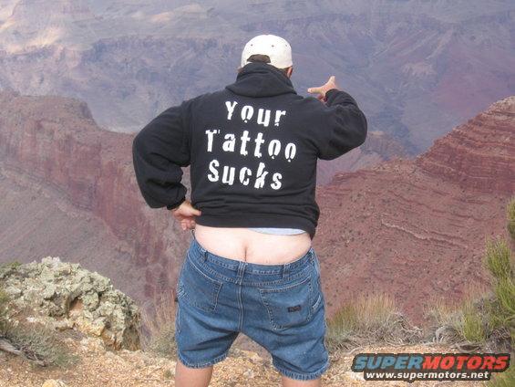 Man in hoodie with "Your Tattoo Sucks" on back, pointing at Grand Canyon