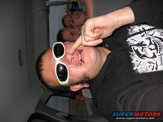 Interior view of a vehicle with people, one person wearing white sunglasses and nose piercings