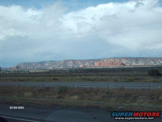 Desert landscape with mesas under a cloudy sky, highway in foreground