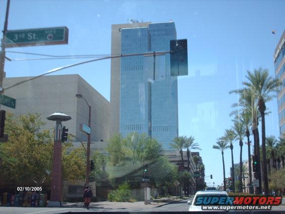 Street sign for 3rd St. and 300 E. with a modern glass skyscraper and palm trees under a clear blue sky