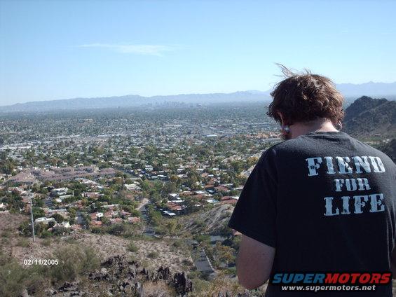 Person wearing a black t-shirt with 'FIEND FOR LIFE' printed on the back, overlooking a city and mountains under a clear blue sky. Date stamp '02/11/2005' visible