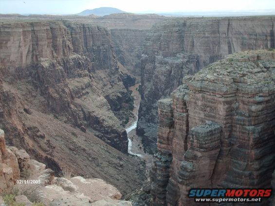 Canyon landscape with river below and mountain in distance. Watermark reads SUPERMOTORS