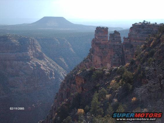 Canyon landscape with layered rock formations and distant mesa under a hazy sky