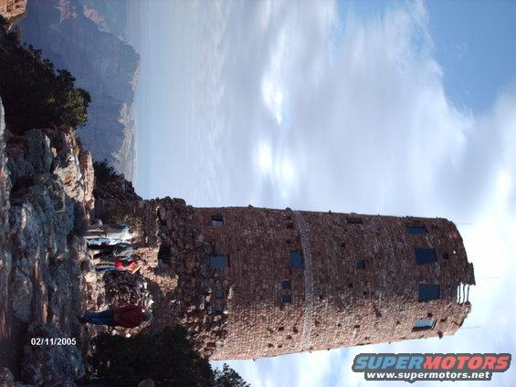 Stone tower on cliff edge overlooking a canyon, with people standing nearby