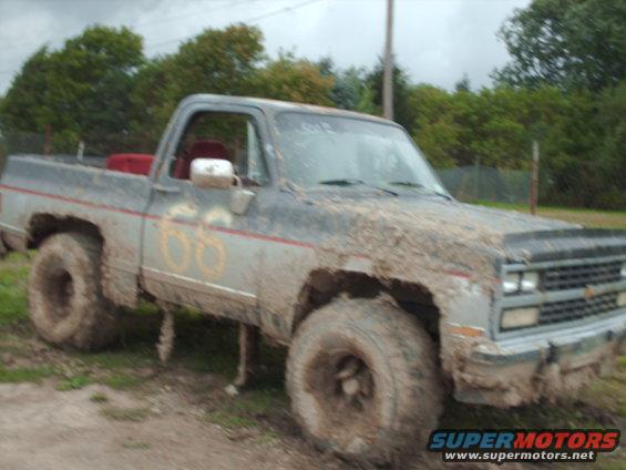 Mud-covered pickup truck with large tires, number 66 on the door, and red interior