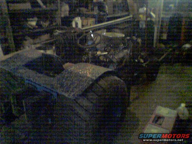 Car interior with dashboard and steering wheel visible, engine block in background. Garage setting