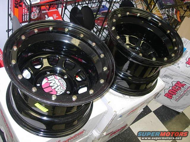 Two black off-road wheels with red and white center caps. Boxes labeled "Rock Crawler" are in the background