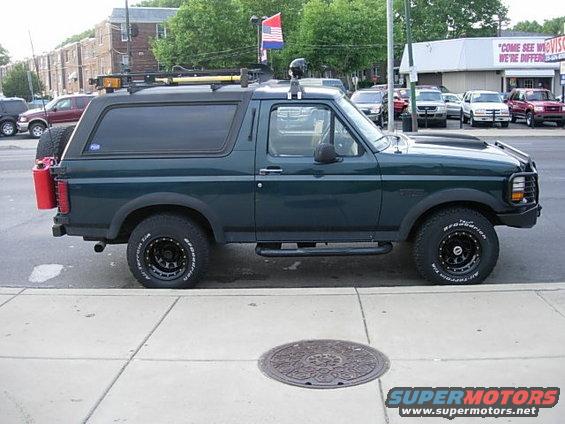 Dark green Ford Bronco with a roof rack, spare tire, and red gas can on the back