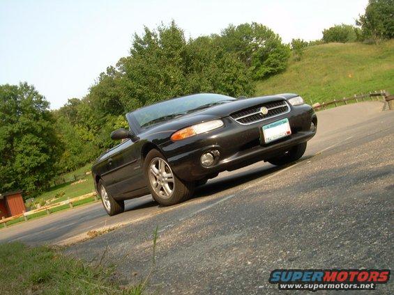 Black convertible parked on the side of a road with trees in the background