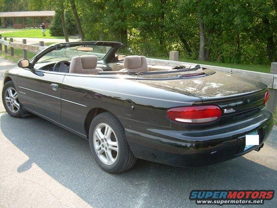 Black convertible parked on pavement, trees and picnic shelter in background