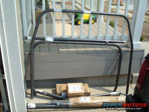 Roll cage tubing and brackets on a wooden deck, with boxes and packaging