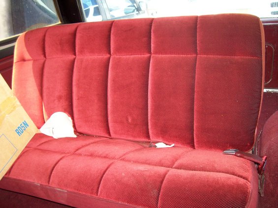 Red velour bench seat with quilted pattern and visible seatbelt buckle. Cardboard box with text 'RD5N' is on the left