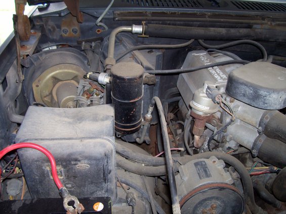 Engine bay with battery, air conditioning components, and engine parts visible