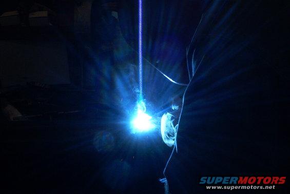 Welding arc with blue light and sparks, dark background, Supermotors.net logo