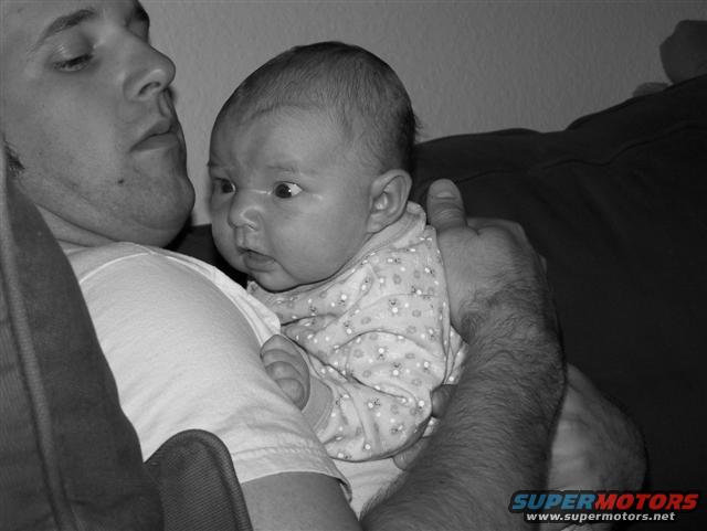 Baby in a patterned onesie held by a man, close-up, black and white