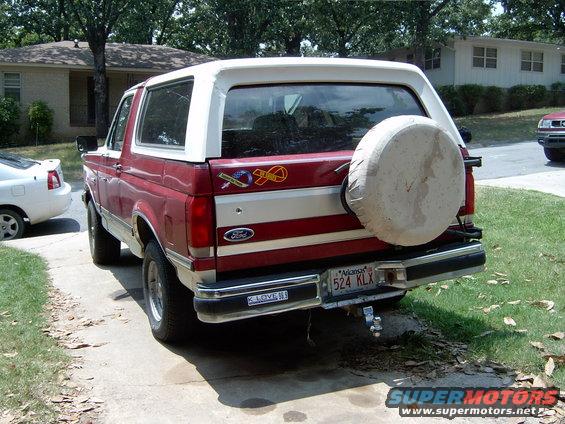Red Ford Bronco with white top, spare tire on back, parked in driveway
