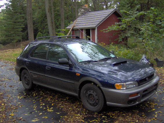Dark blue 1997 Subaru Impreza wagon with a hood scoop and roof rack parked on a driveway with fallen leaves