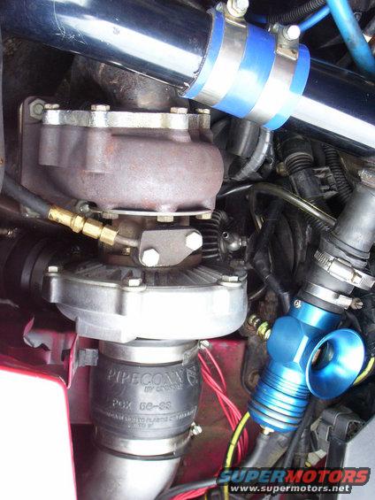 Close-up of a turbocharger with blue silicone couplers and intake piping. Text on a rubber hose reads 'PIPECONX'