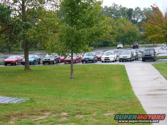 Several cars parked in a lot, including a white Subaru WRX