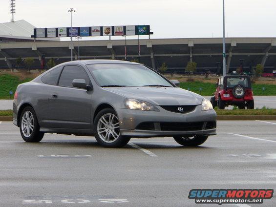 Gray coupe, 3/4 front view, with a red Jeep in the background