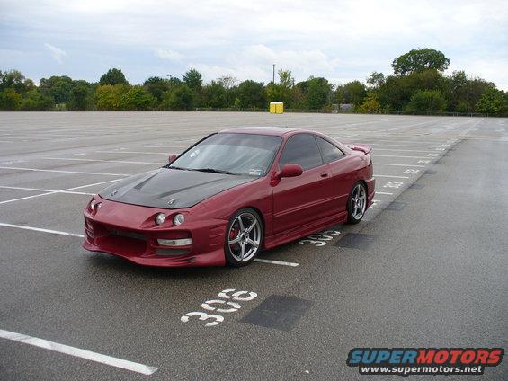 Red coupe with aftermarket carbon fiber hood and spoiler parked in a lot