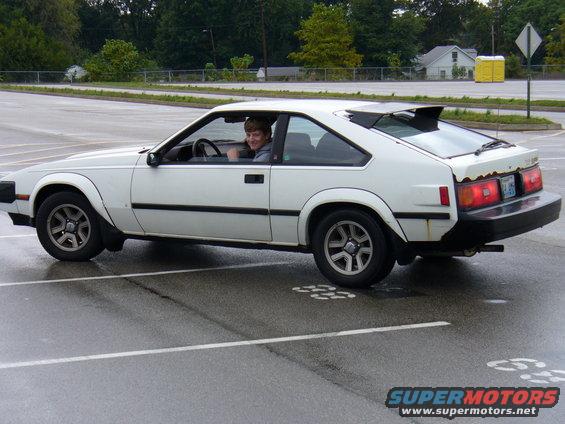White coupe with a spoiler and rust on the rear bumper, seen from the side
