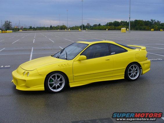 Yellow coupe with aftermarket body kit and silver wheels parked in an empty lot