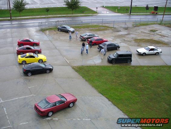 Red coupe parked in a lot with other cars and people