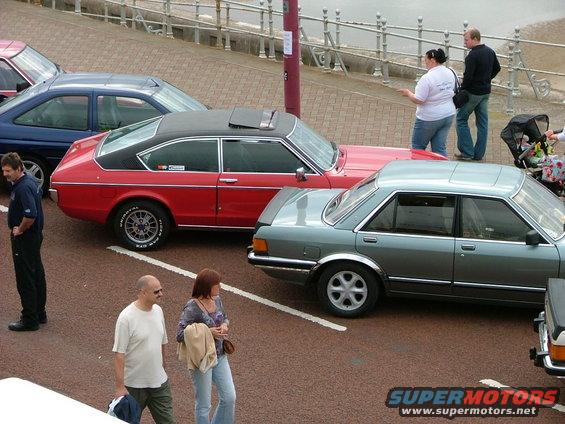 Red coupe with black roof and grey sedan parked side-by-side