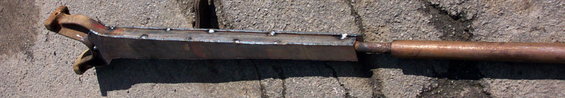 Welded metal tool with a copper pipe handle, resting on concrete