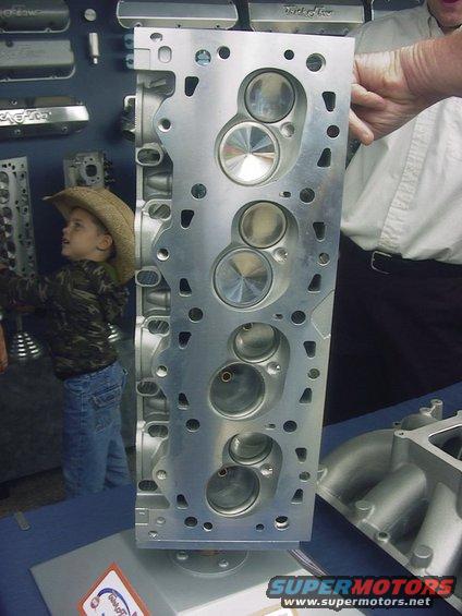 Aluminum engine cylinder head with valves visible, a child in a cowboy hat looks on