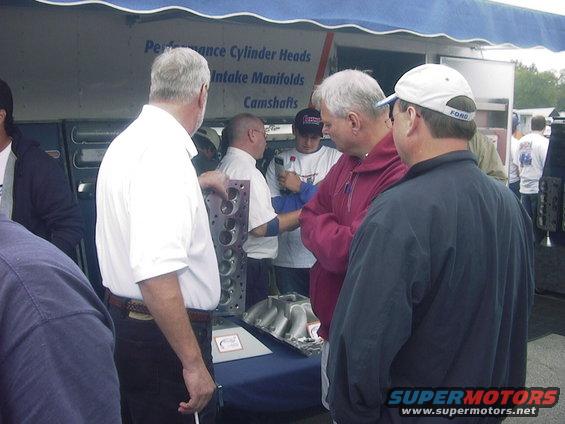 Engine cylinder head and intake manifold on display table with people around