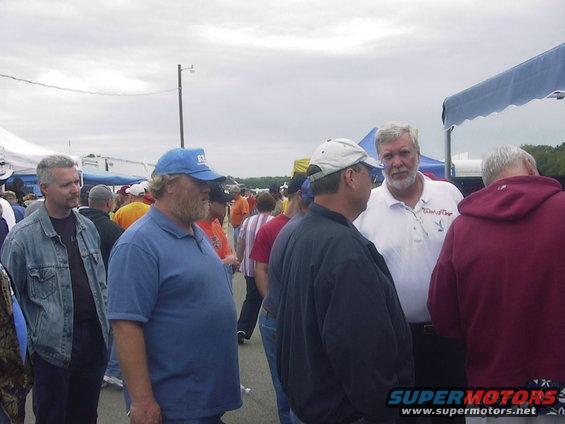 Several men in casual clothing stand around at an outdoor gathering, some talking