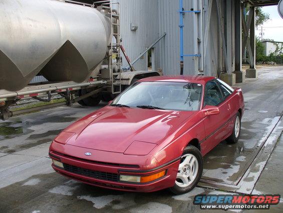 Red 1991 Ford Probe coupe parked in front of an industrial building and tanker truck