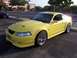 2002 Ford Mustang - A yellow 2002 Ford Mustang is parked in a lot, with a black car visible in the background.