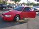 2002 Ford Mustang - A red Ford Mustang with racing stripes is parked in a lot with its driver's door open.