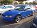 2002 Ford Mustang - A blue Ford Mustang is parked in a lot with other vehicles and trees in the background.